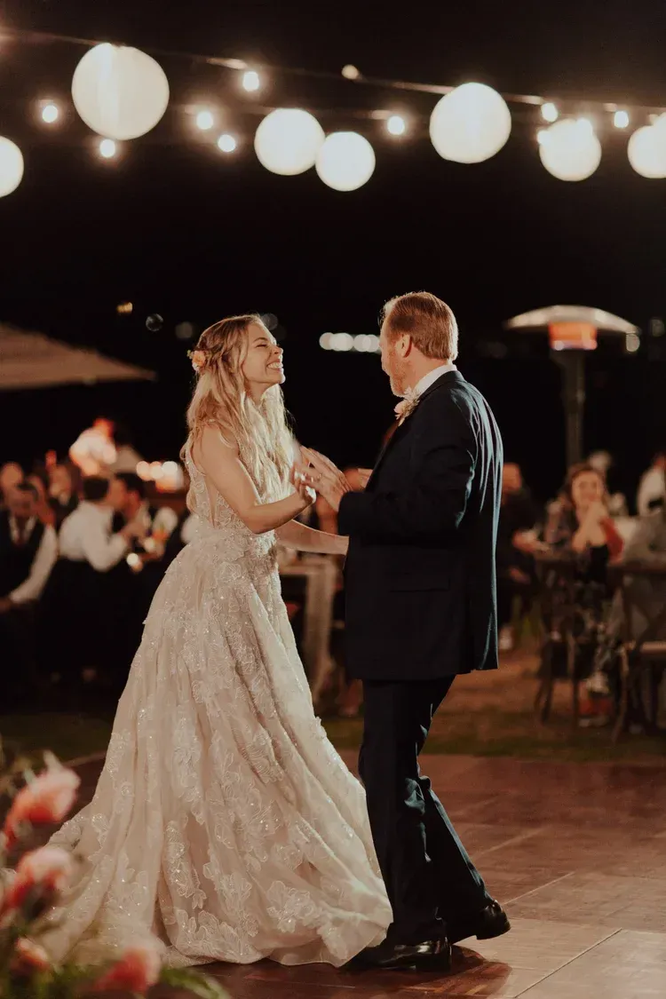 Bride and groom dancing under string lights at an evening wedding reception