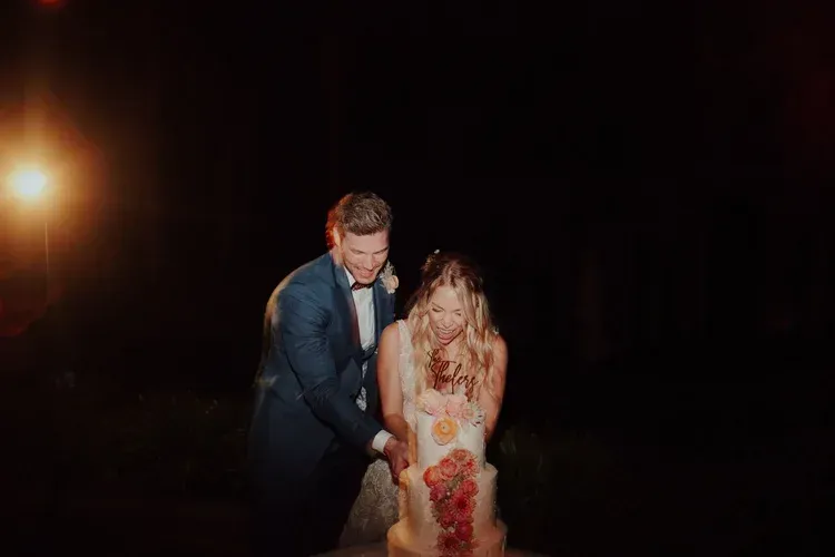 Couple cutting a wedding cake on a dark stage with warm spotlight