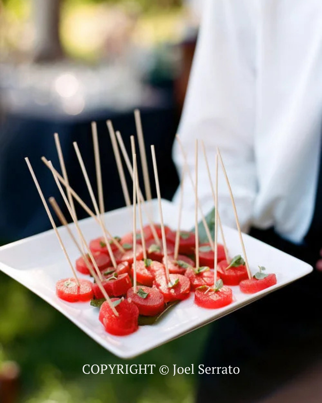Tray of red fruit skewers with wooden picks, held by a person in white at a catered event
