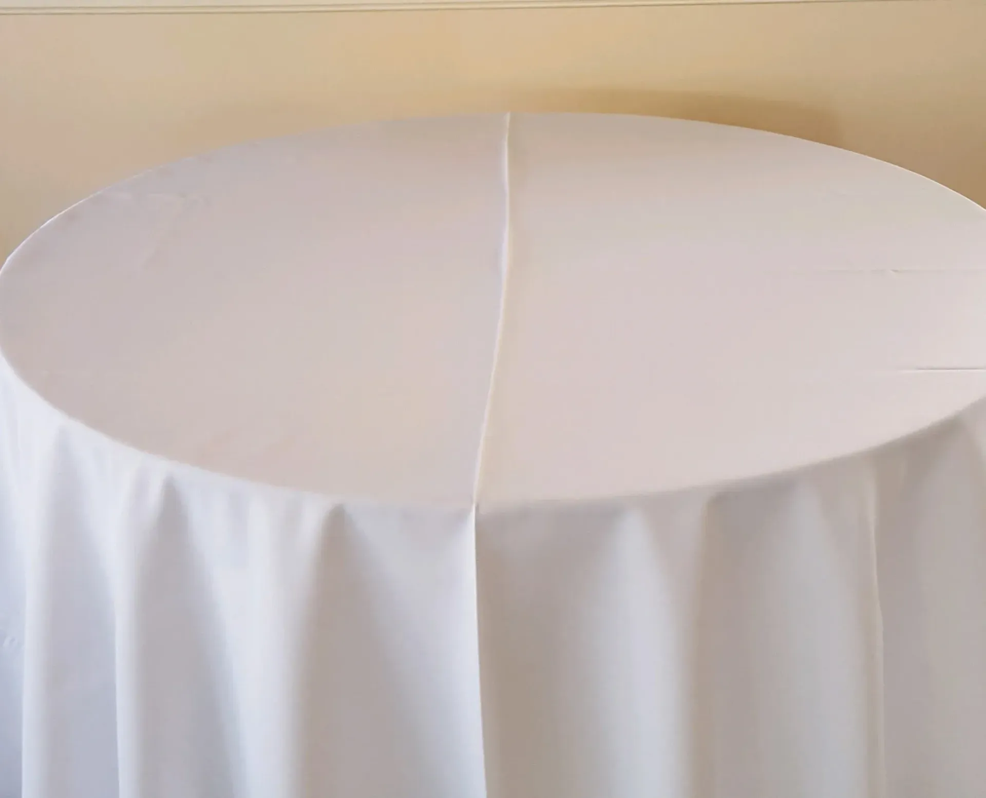 Round table covered in a white tablecloth against a beige background