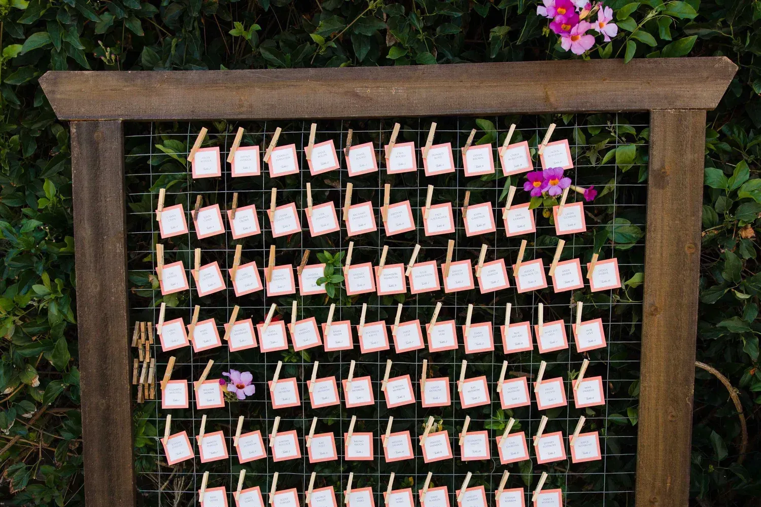 Wooden frame filled with rows of small pink note cards clipped to wire outdoors
