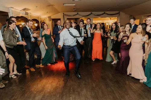 Man dancing at a lively indoor party with guests in formal attire watching around him