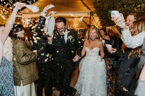 Wedding couple walking through confetti as guests cheer indoors
