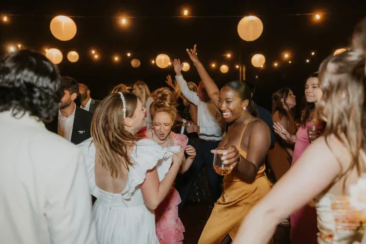 Guests dancing under warm string lights at a lively indoor party.