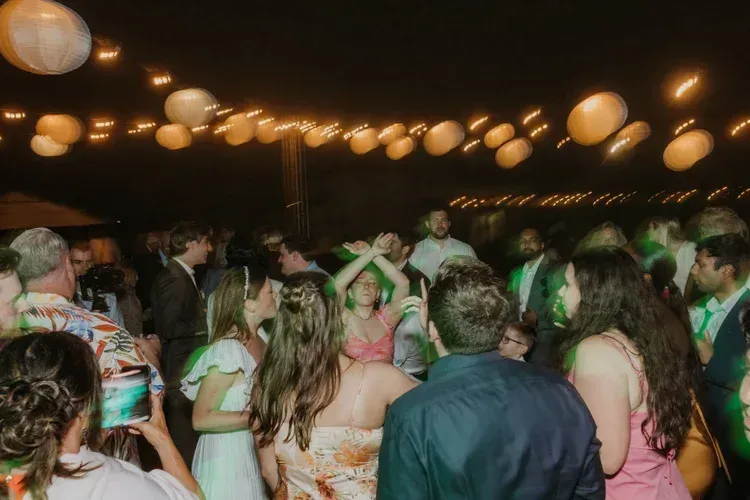 Crowded indoor dance floor under warm hanging lantern lights, people mingling and dancing.