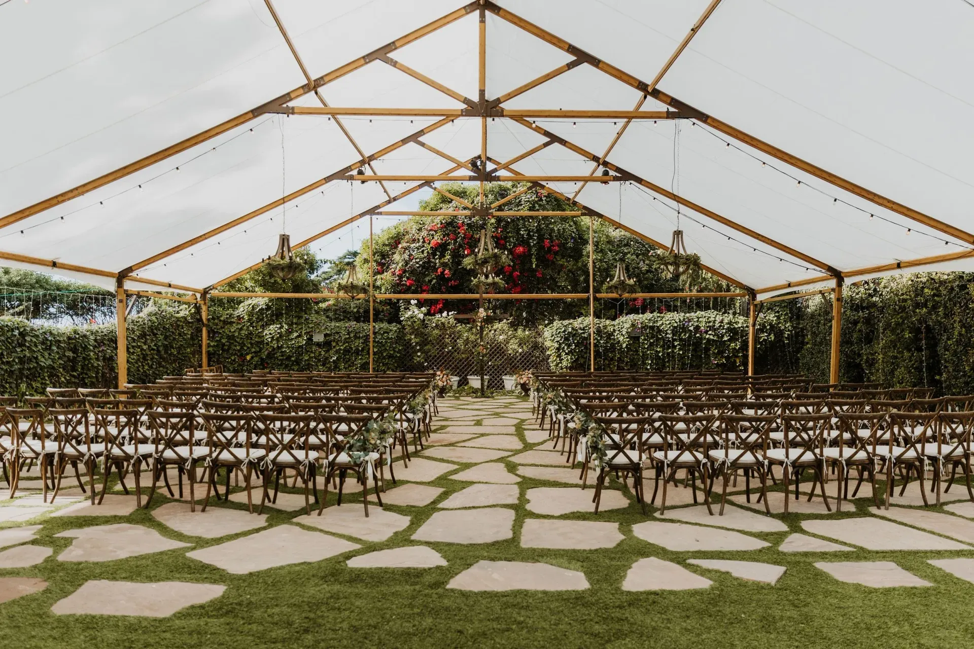 Outdoor wedding setup with rows of chairs under a white tent and stone path leading to greenery