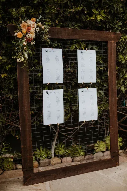 Wooden frame with four hanging white menu sheets and flowers, set against greenery outdoors