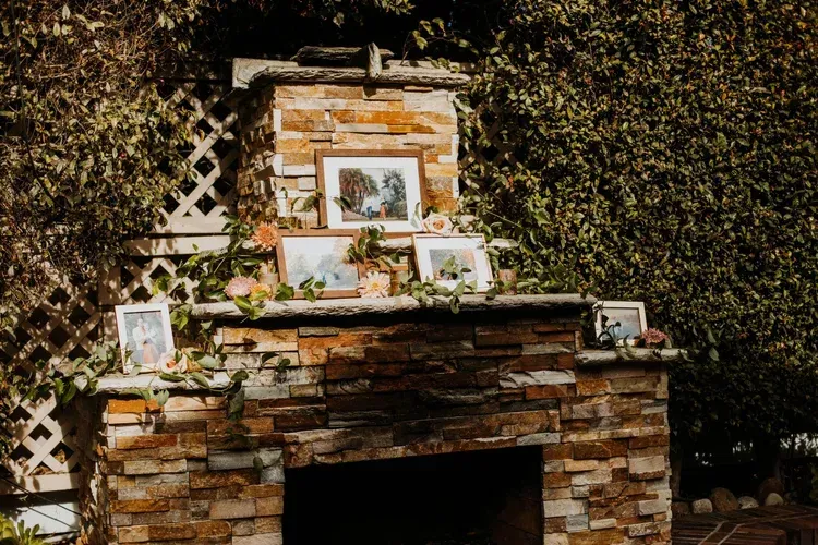 Stone fireplace mantel with framed photos and flowers in a leafy garden setting