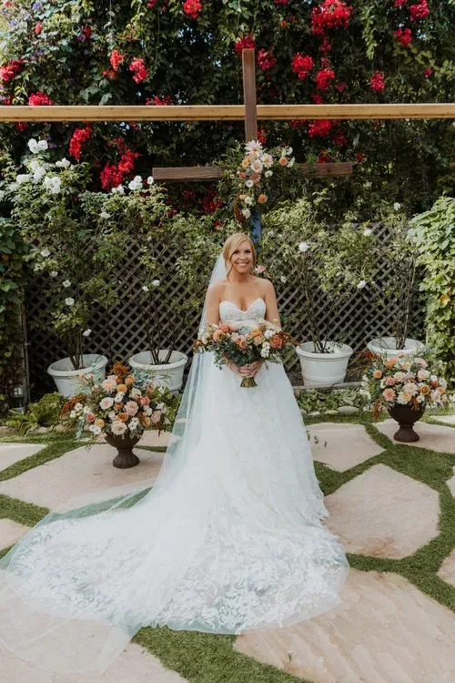 Bride in a white gown holding a bouquet in a flower-filled garden setting.