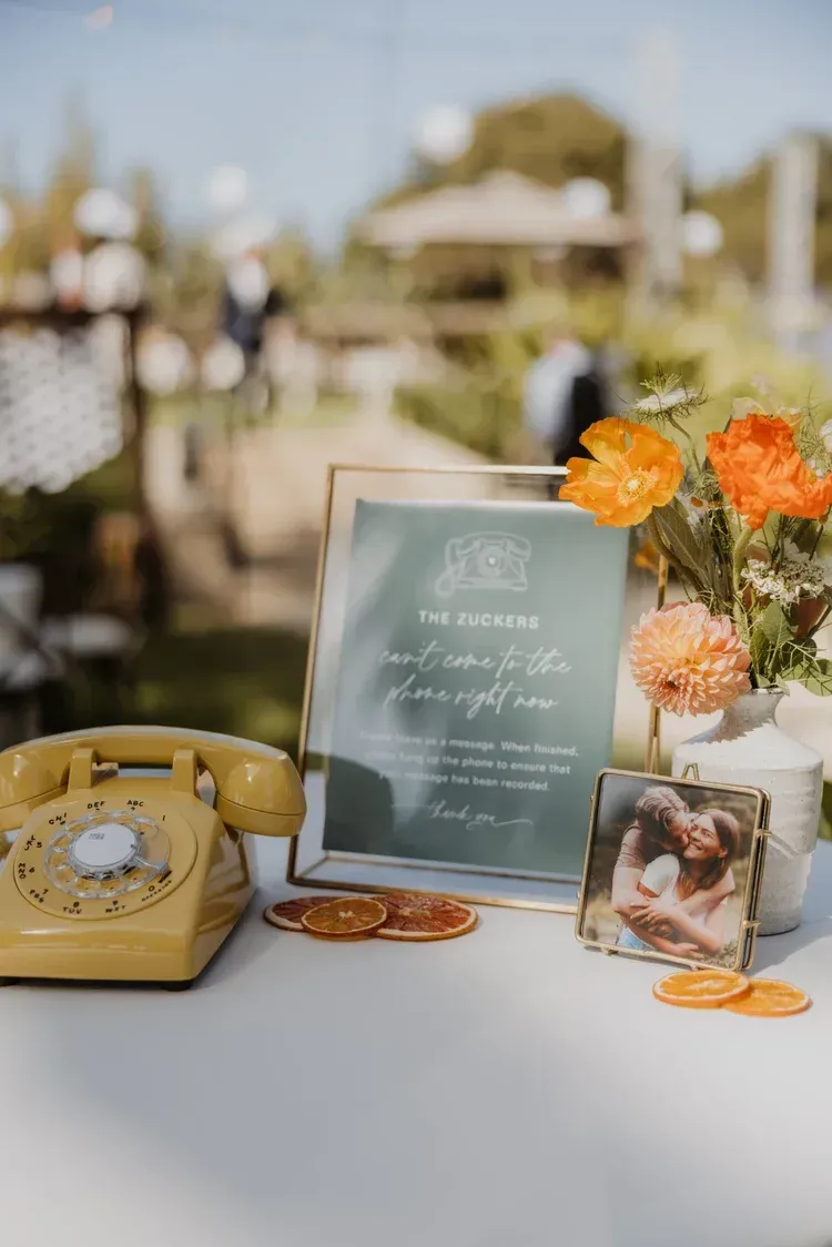 Wedding welcome table with framed sign, yellow rotary phone, flowers, and photo display on a white table
