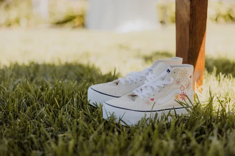White sneakers on grass beside a person’s leg in a sunny outdoor setting