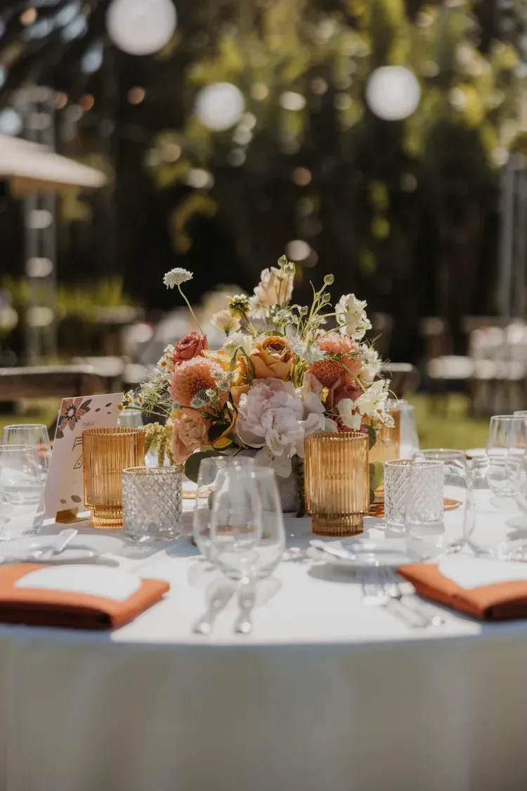 Elegant outdoor dining table with floral centerpiece, glassware, and folded napkins in warm sunlight