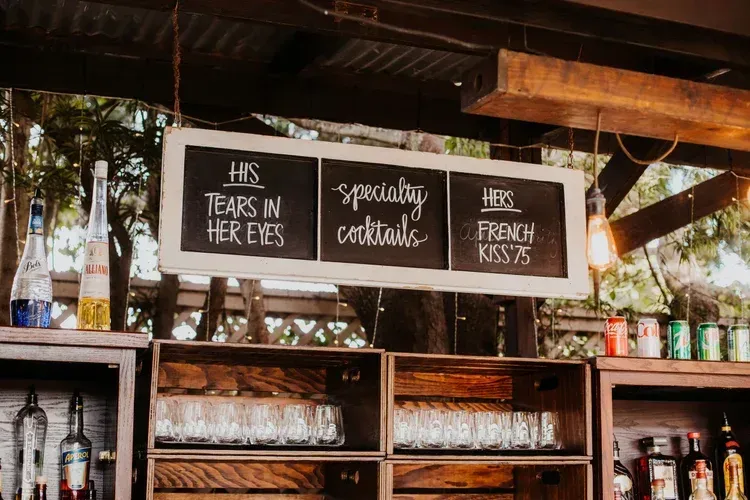 Bar shelves and chalkboard sign advertising tears in her eyes, specialty cocktails, and French 75s