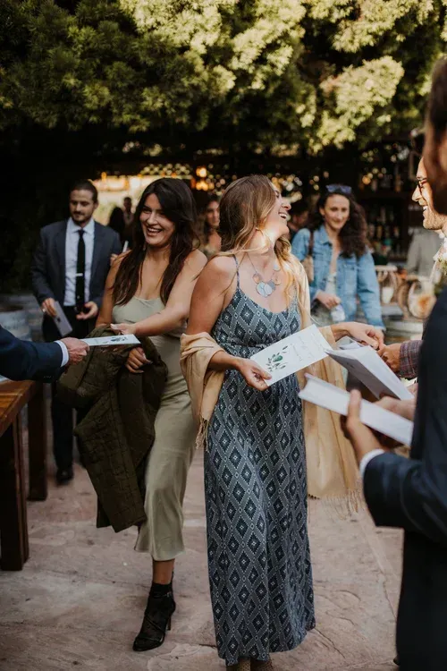People mingling outdoors at a formal gathering, holding papers and smiling under trees.