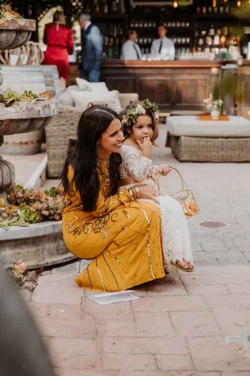Two women in yellow and white dresses sitting outdoors at a market café, smiling and chatting