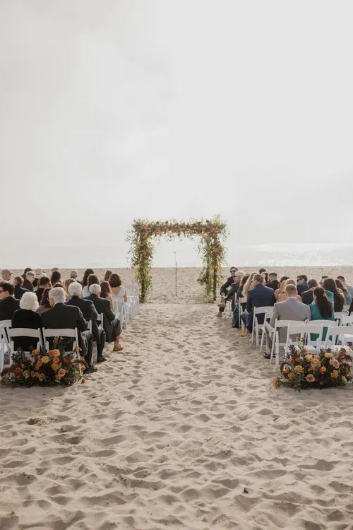 Beach wedding ceremony setup with guests seated facing a floral arch by the ocean