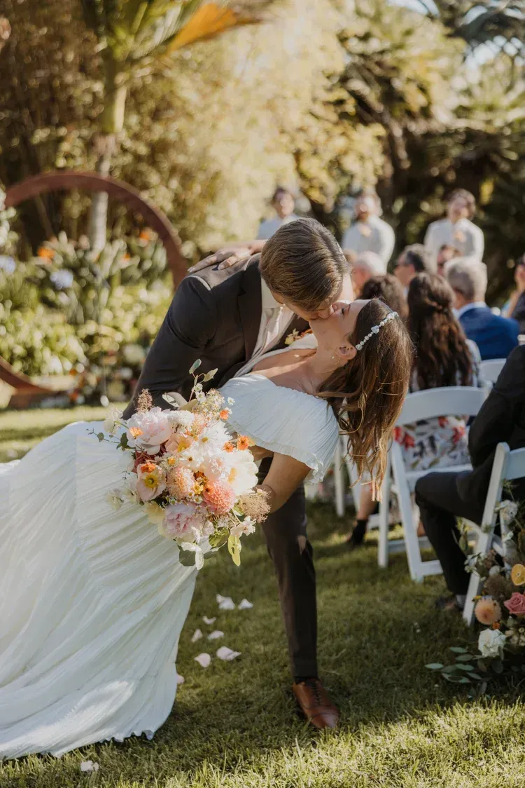 Bride and groom kissing at an outdoor wedding, with a bouquet in the foreground.