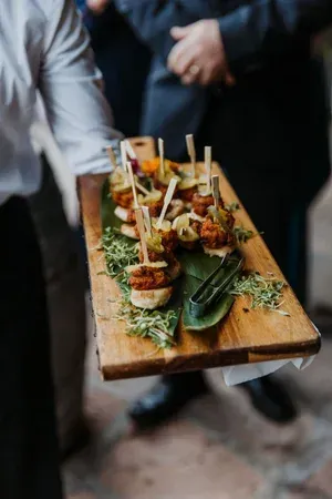 Tray of assorted appetizers on a wooden board, carried by a server in a blurred indoor setting