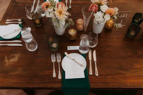 Elegant dining table set with white napkins, green accents, candles, and floral centerpieces.