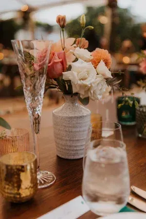 Floral centerpiece on a candlelit dinner table with wine glasses and water glasses outdoors