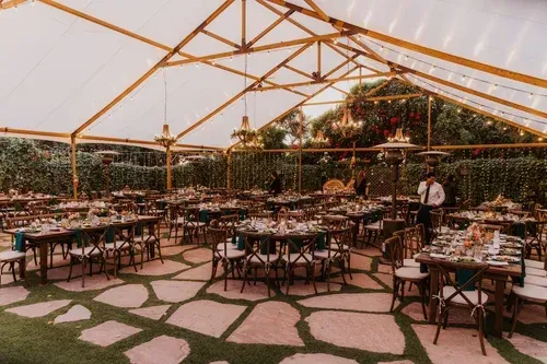 Outdoor dining tent with long tables and chairs under a white canopy, surrounded by greenery