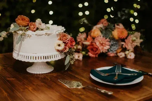 Wedding cake with peach roses on a wooden table, with teal plates and floral decor in the background
