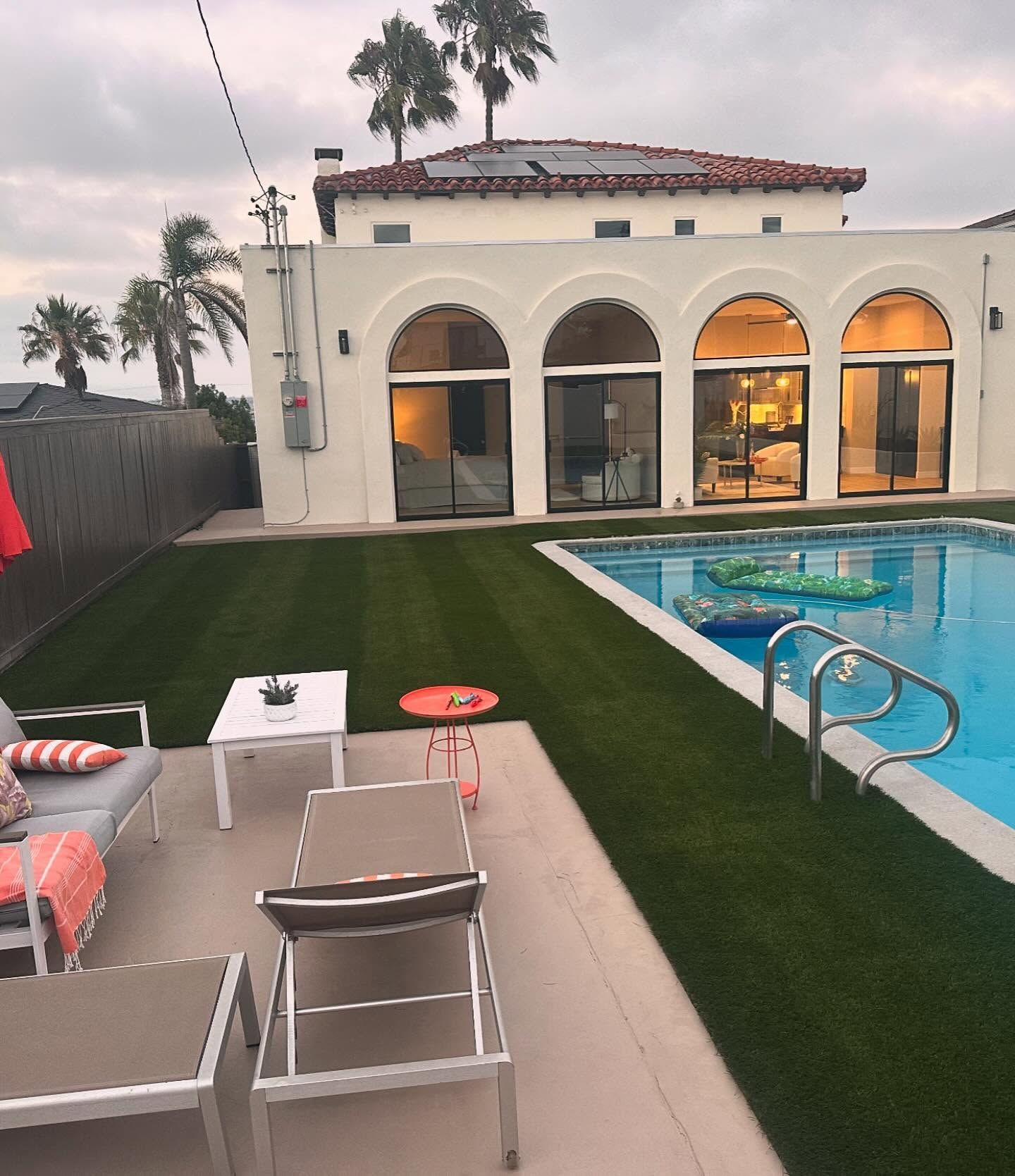 Backyard patio with a swimming pool, lounge chairs, and a white house with arched doors and windows