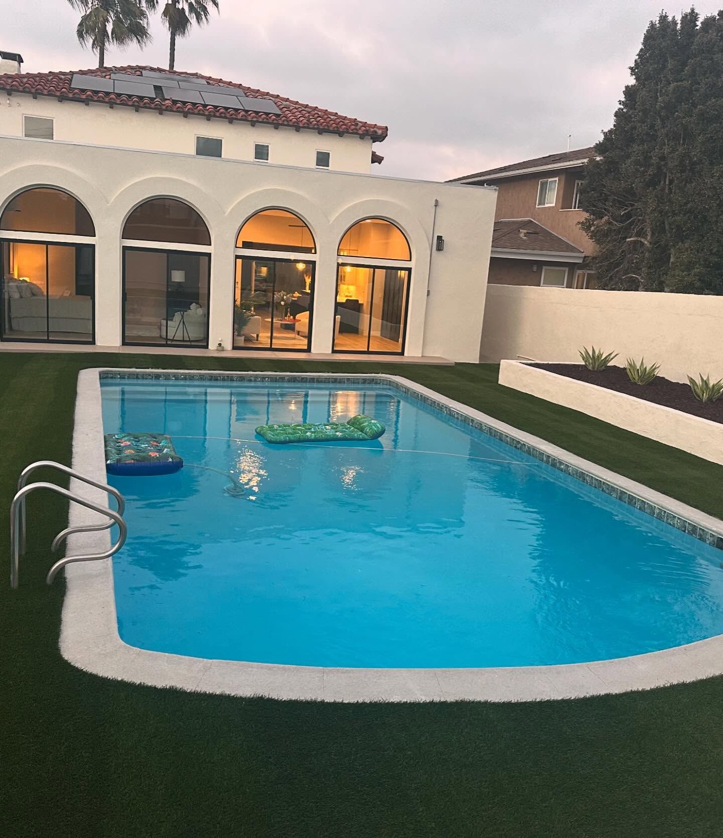 Backyard swimming pool beside a cream stucco house with arched windows at dusk