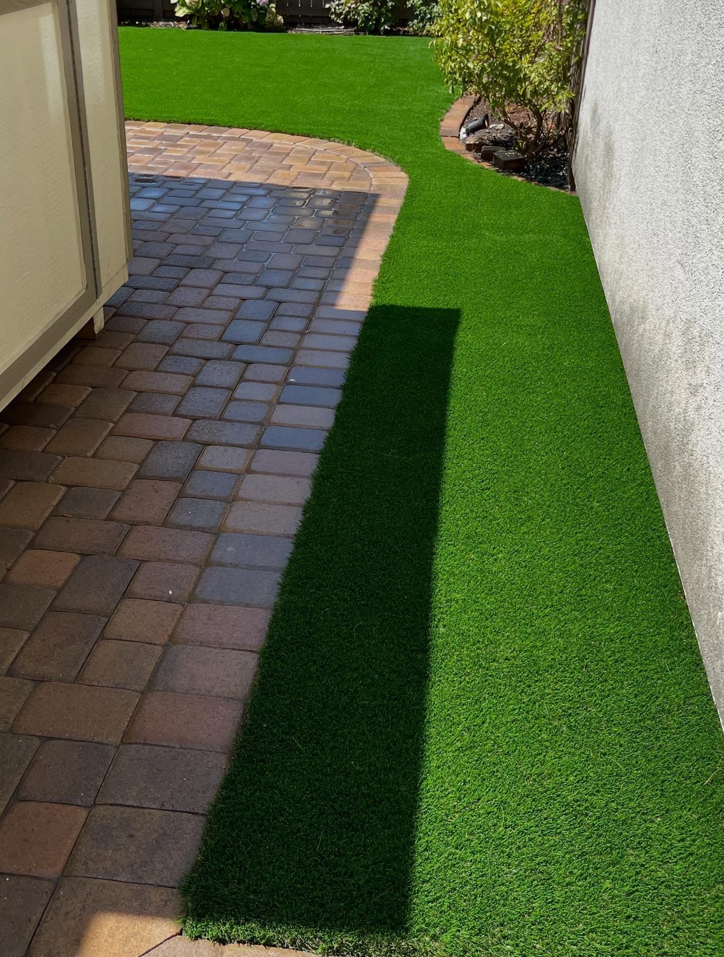 Brick patio beside a narrow strip of bright green turf along a house wall