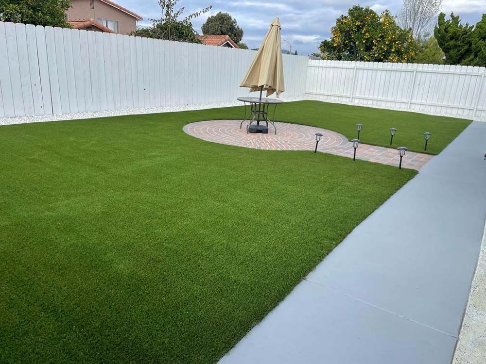 Backyard with green lawn, white fence, patio umbrella, and paved walkway.
