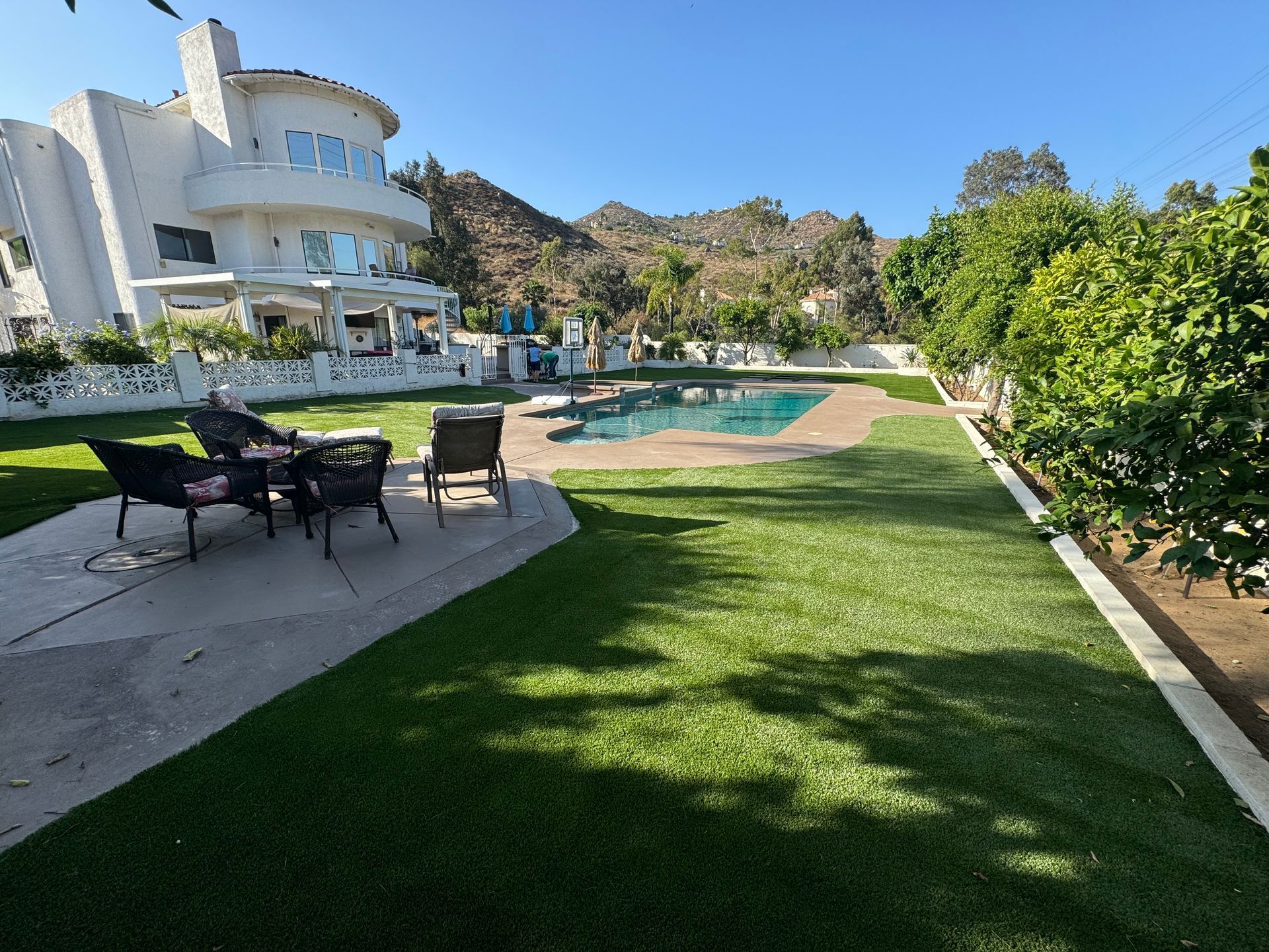 Modern white house with a pool, patio seating, and a green lawn under a clear blue sky
