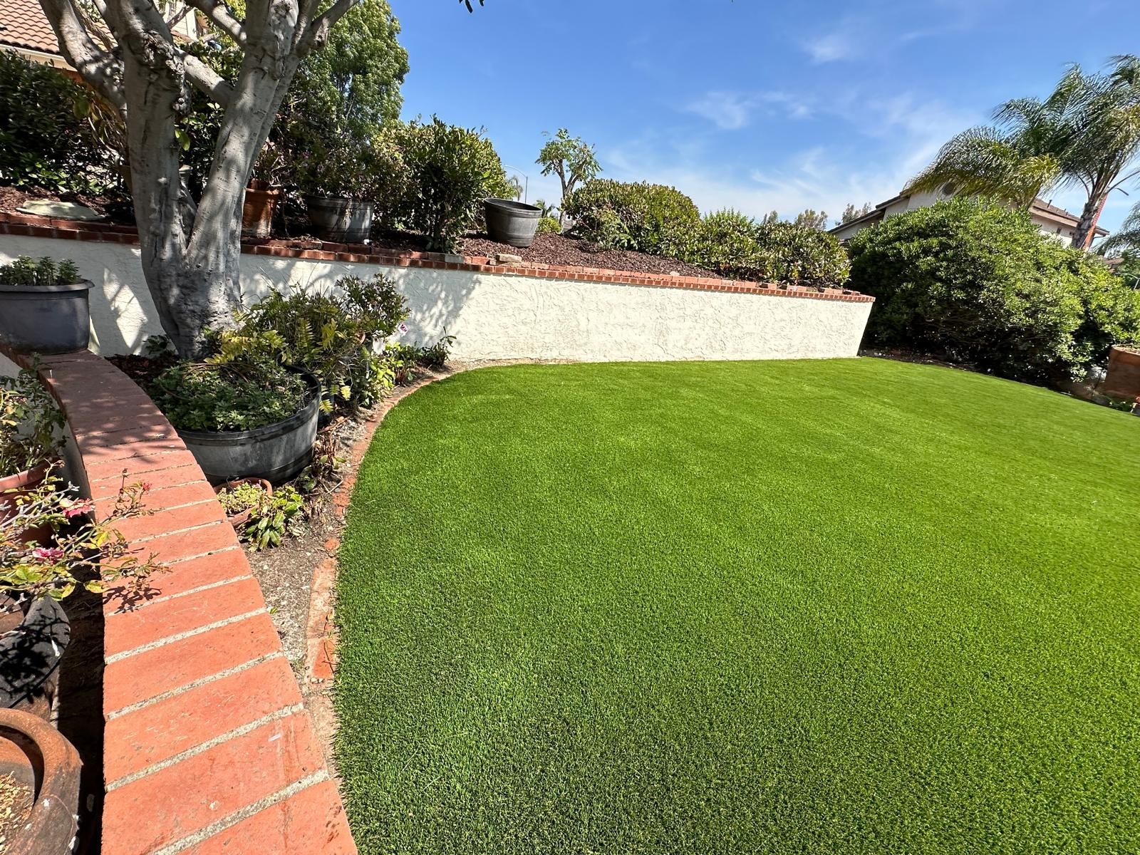 Curved brick path beside a lush green lawn and white stucco wall in a sunny garden