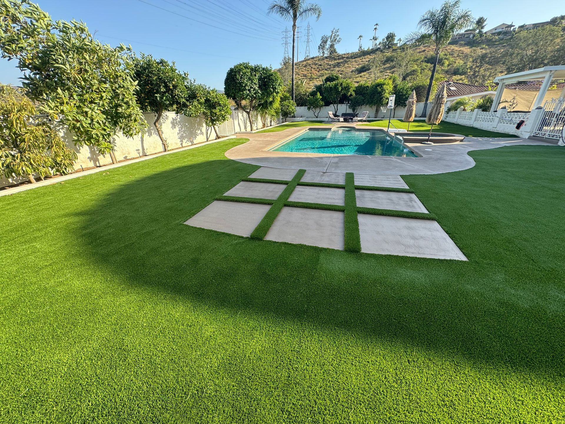 Backyard with green lawn, stone stepping pads, and a swimming pool under a clear blue sky.
