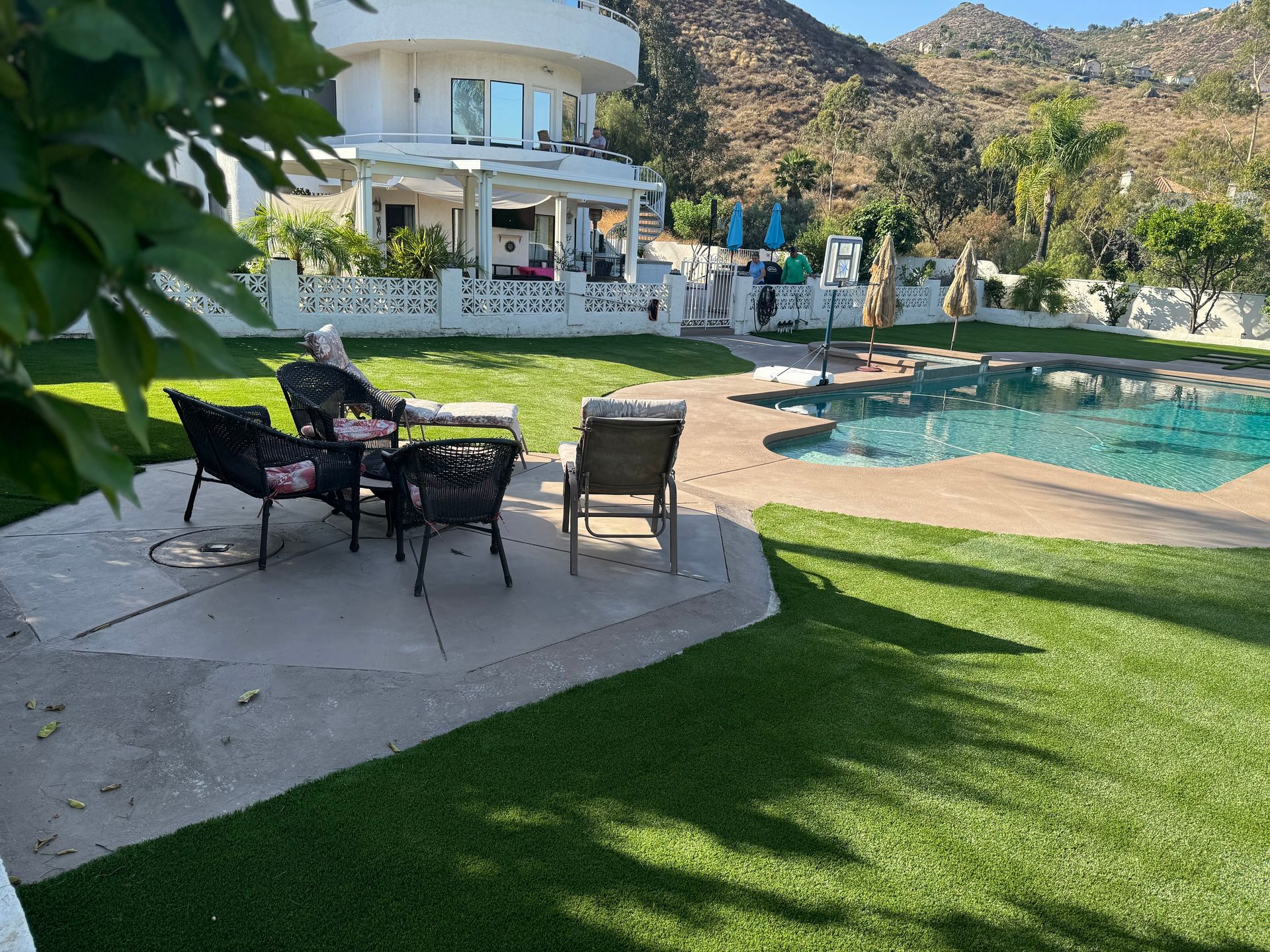 Backyard patio with chairs by a swimming pool and a white house in a desert hillside setting