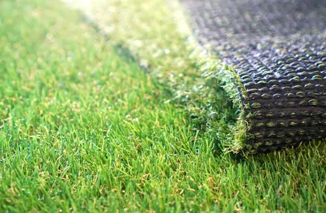 Close-up of artificial turf being rolled out on a grassy surface