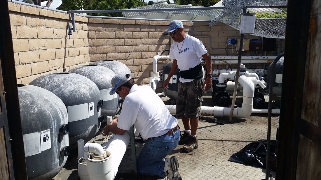 Two men are working on a pipe outside of a building