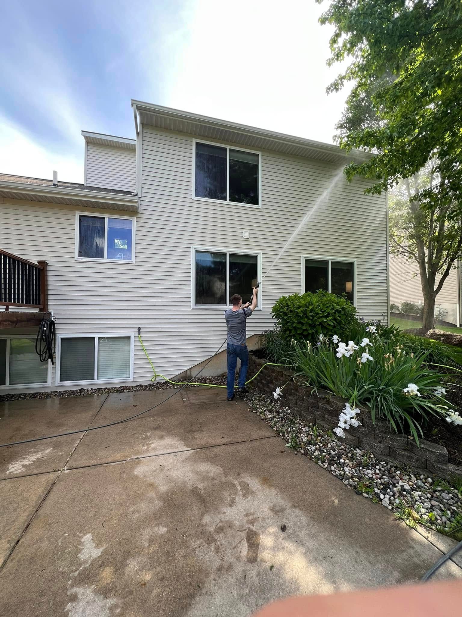 Person standing by beige house with diamond-pattern siding and front garden, under cloudy sky