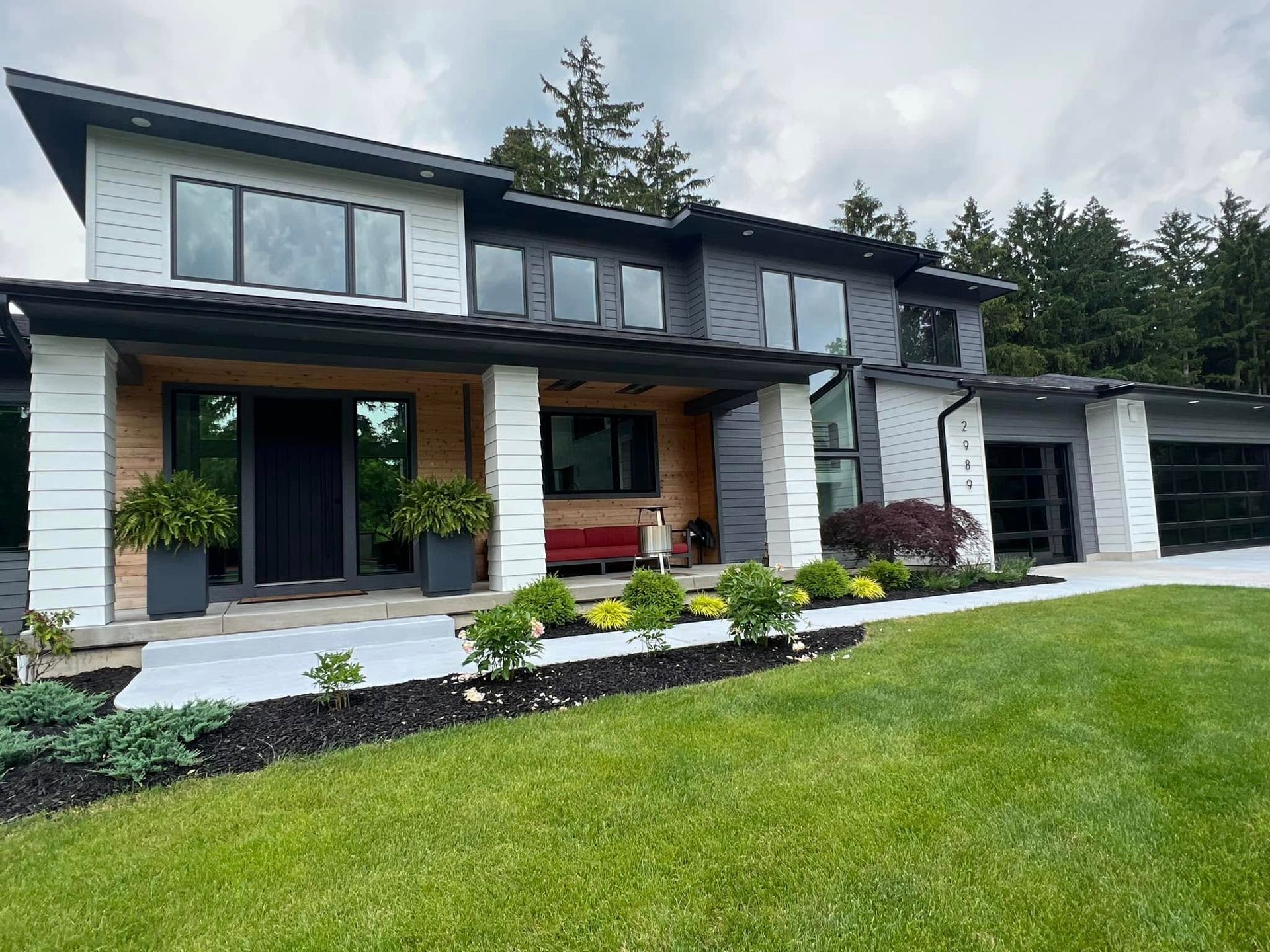 Modern two-story house with a covered porch, dark trim, and a green lawn in front