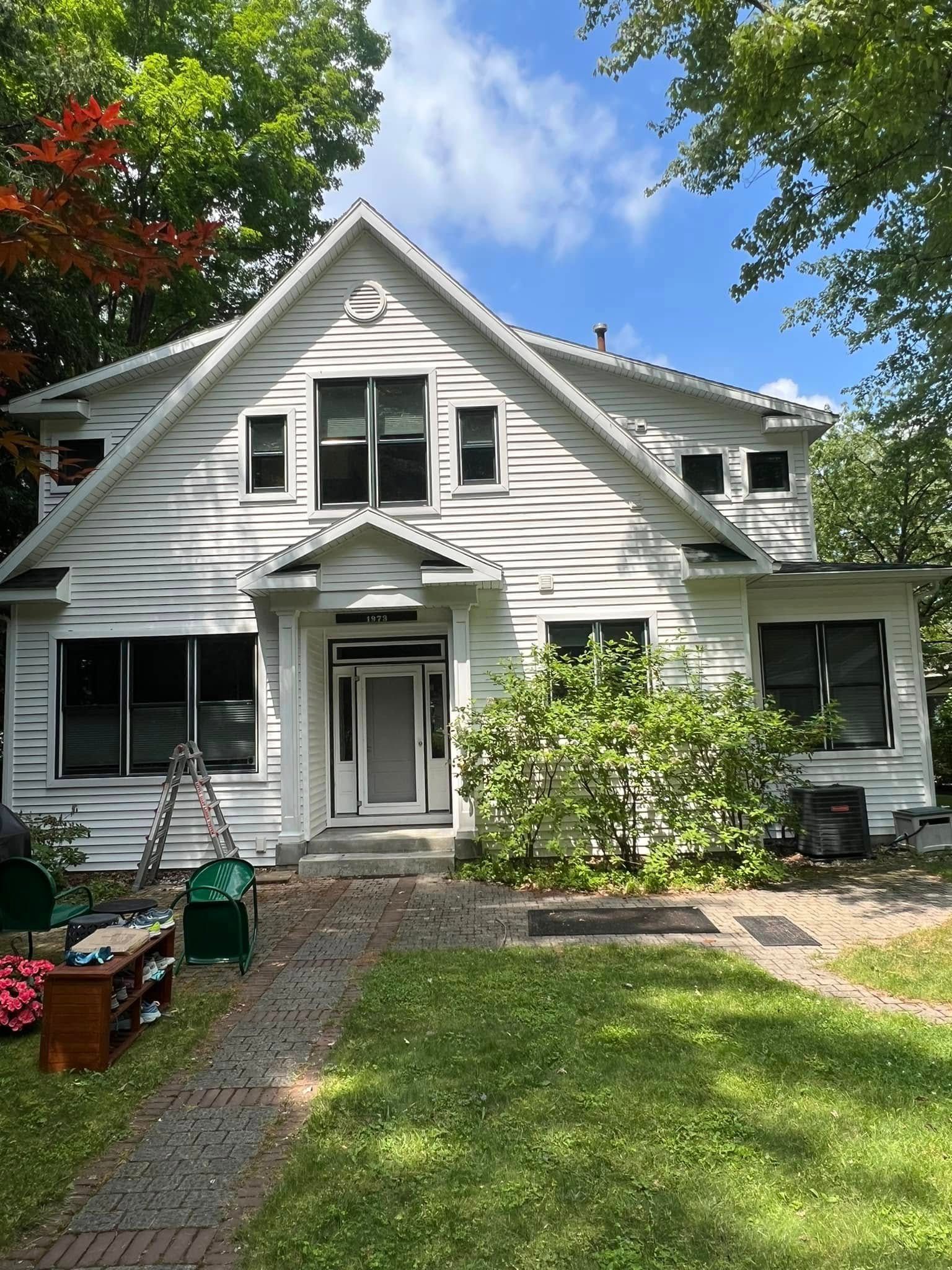 White two-story house with front porch, green lawn, and trees under a blue sky
