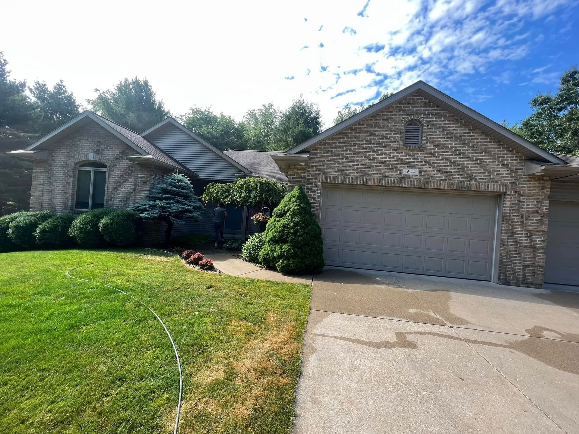 Suburban brick house with attached garage, green lawn, and curved driveway under a sunny sky