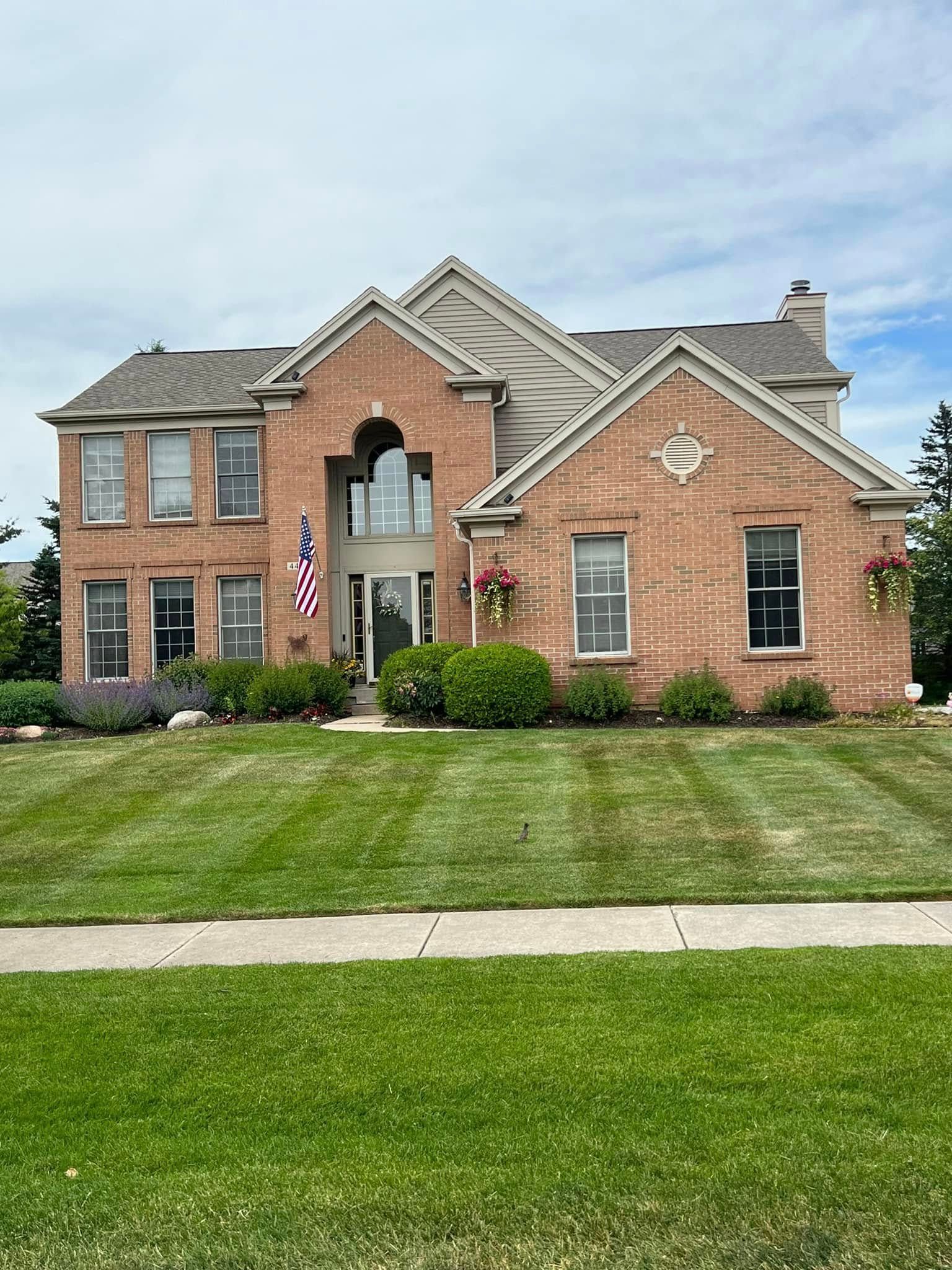 Large brick suburban house with a manicured lawn and a flag by the front door