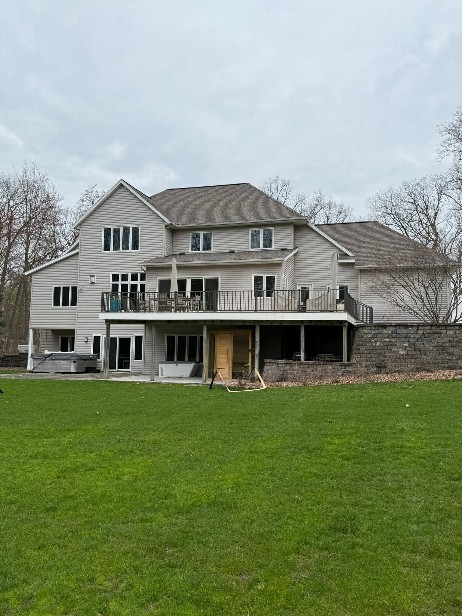 Large beige house with a covered porch and green lawn under a cloudy sky