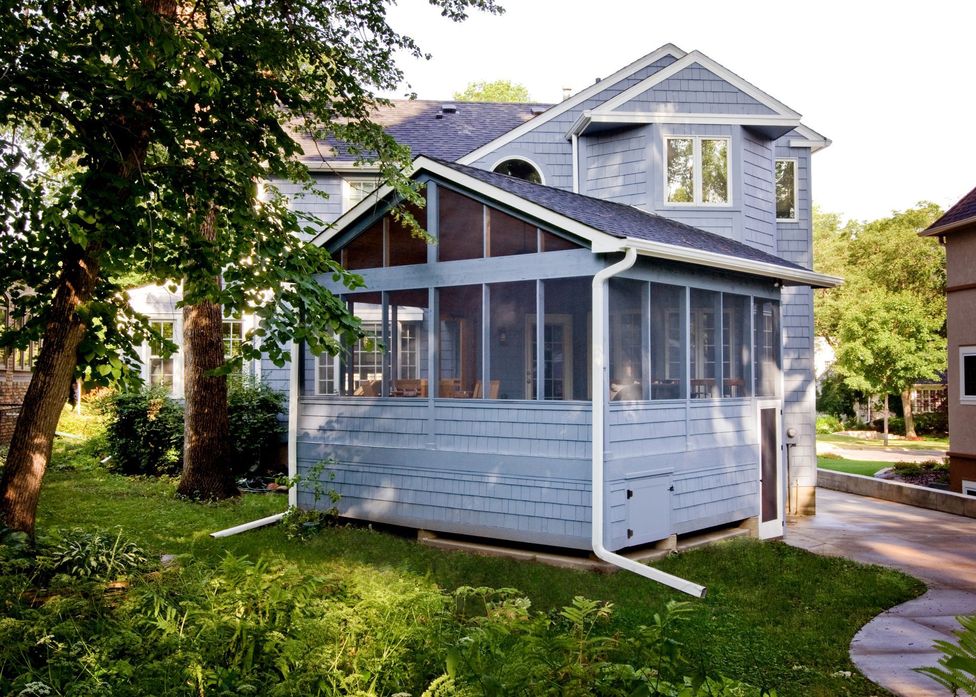 Gray-blue house with a screened porch, red steps, and tall trees in a fenced yard