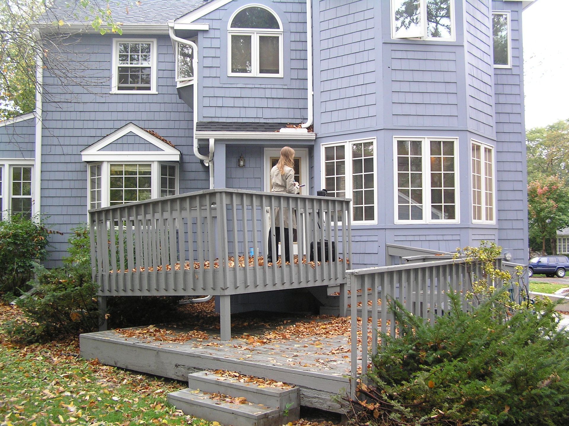Gray house entry with a white-framed glass door, porch light, and fallen leaves on the steps