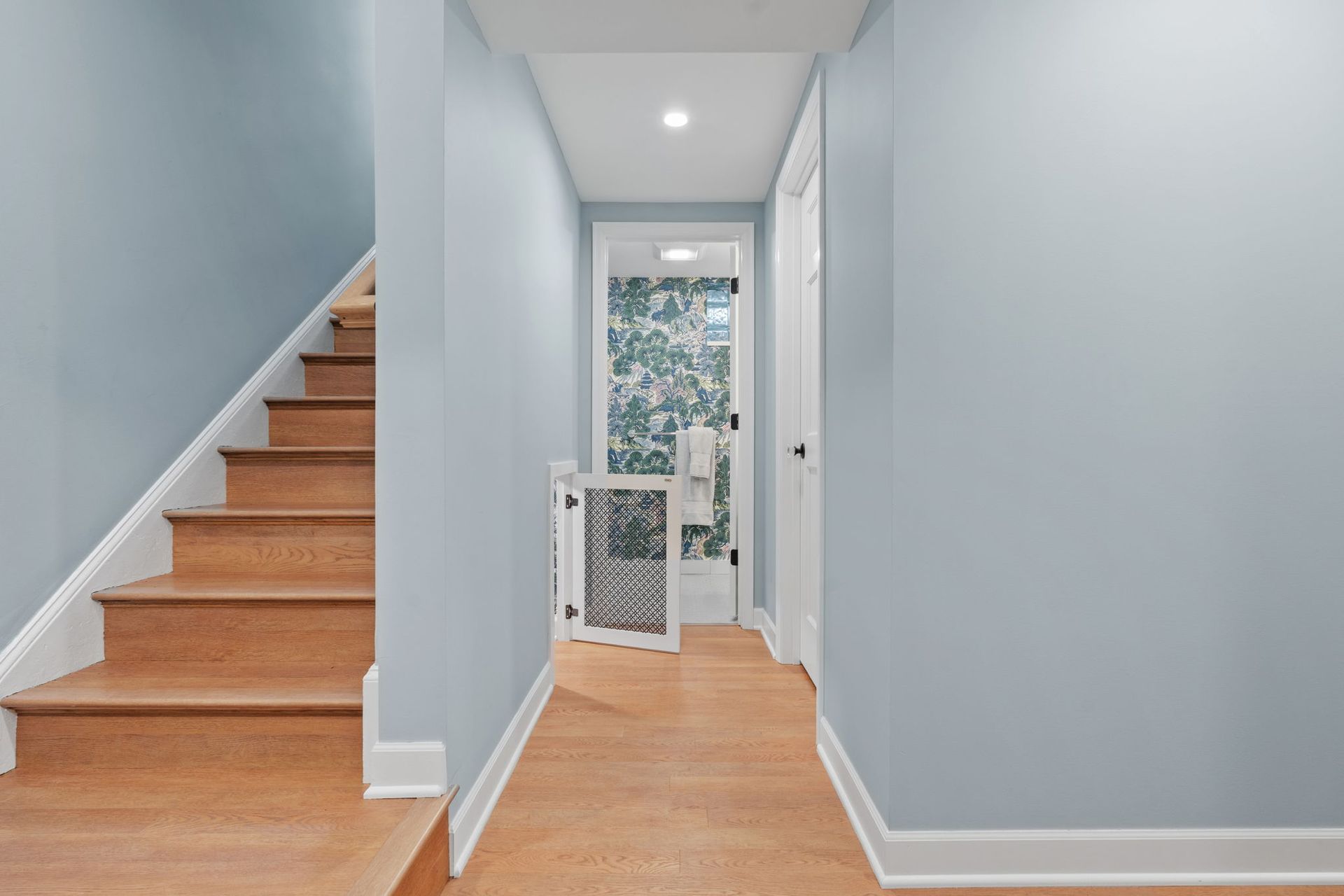 Carpeted staircase with white walls and wooden banister in a narrow hallway