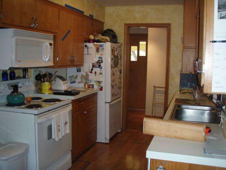Small kitchen with white appliances, wooden cabinets, and a counter with a cutting board.
