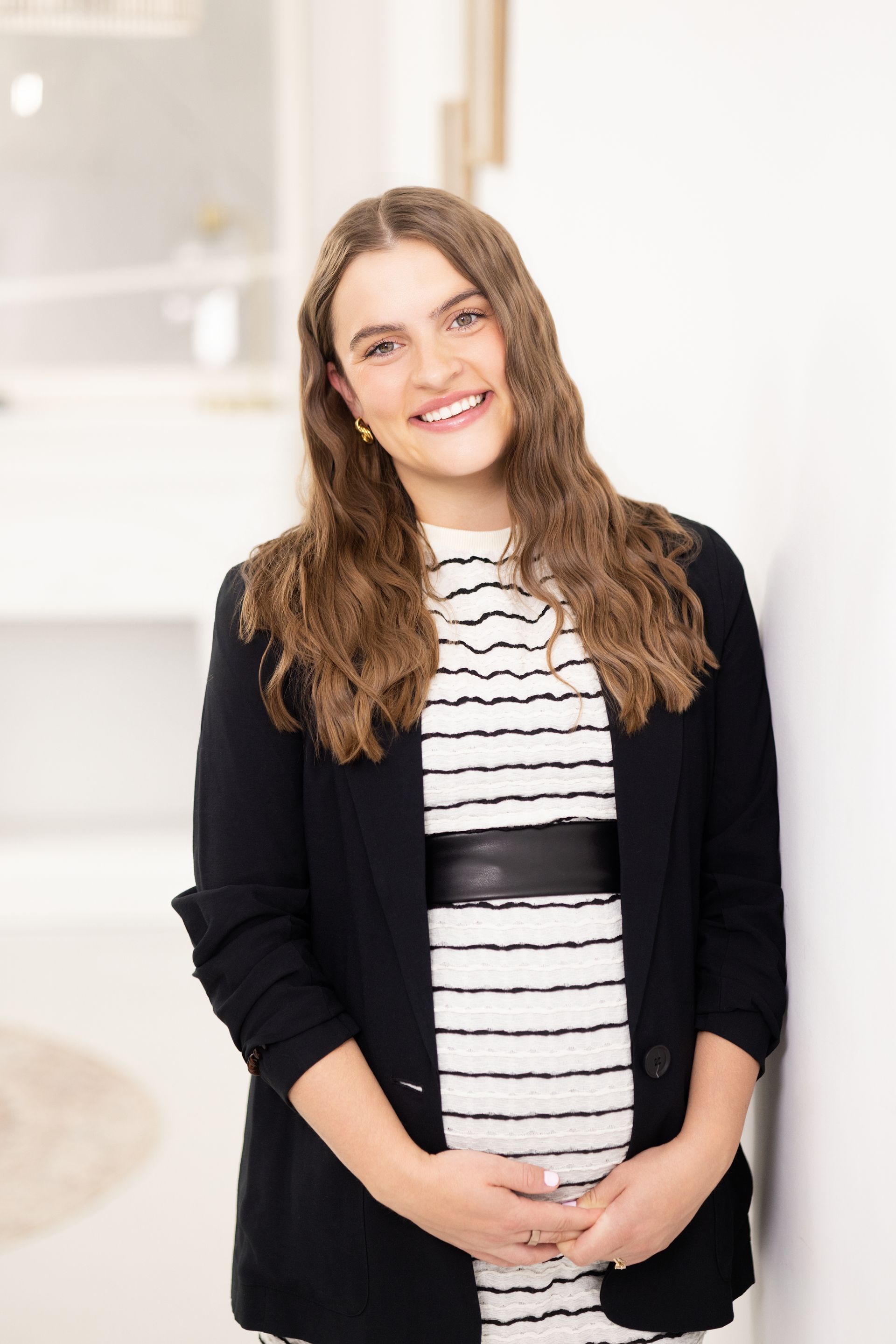 Smiling person in a white blouse and hoop earrings standing indoors with arms crossed