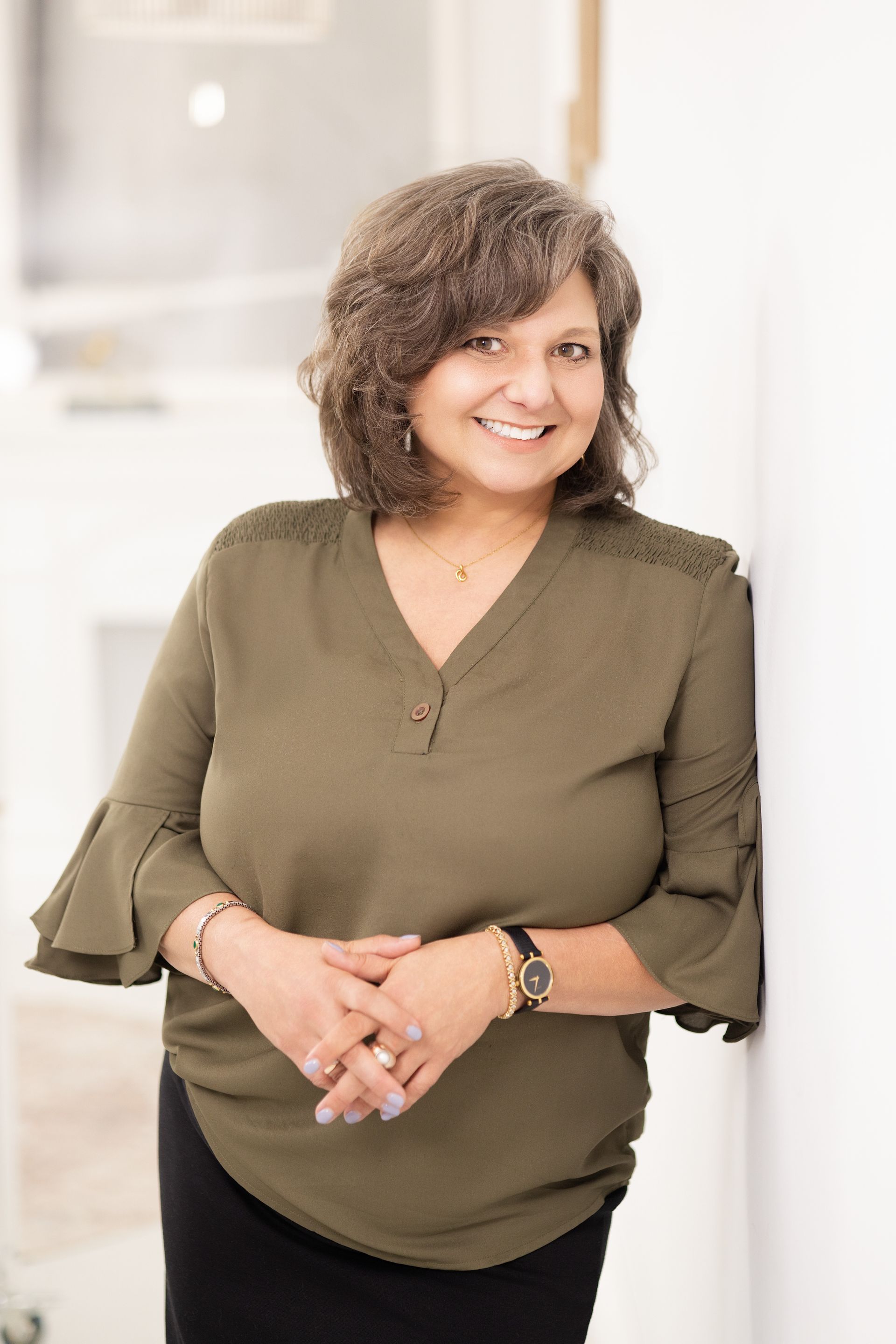 Smiling person with wavy brown hair in a gray shirt, posed against a bright white background