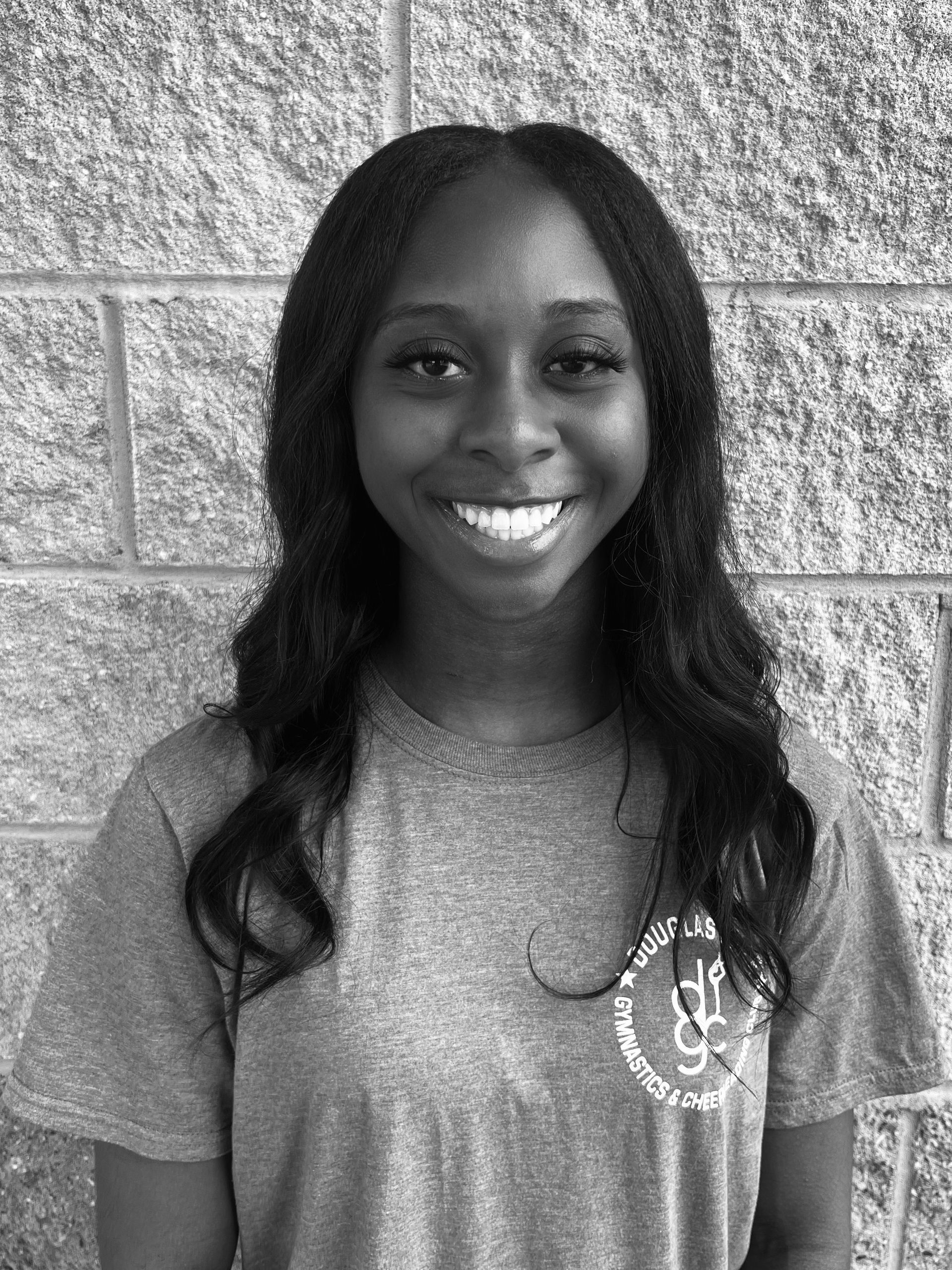 A black and white photo of a woman smiling in front of a brick wall.