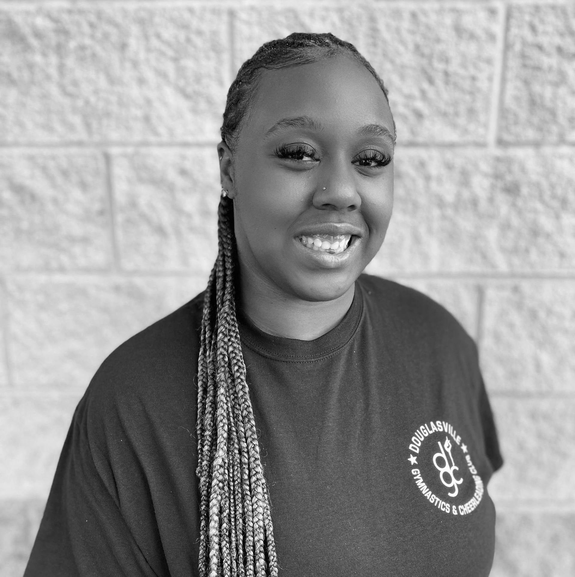 A woman in a black shirt is smiling in front of a brick wall.